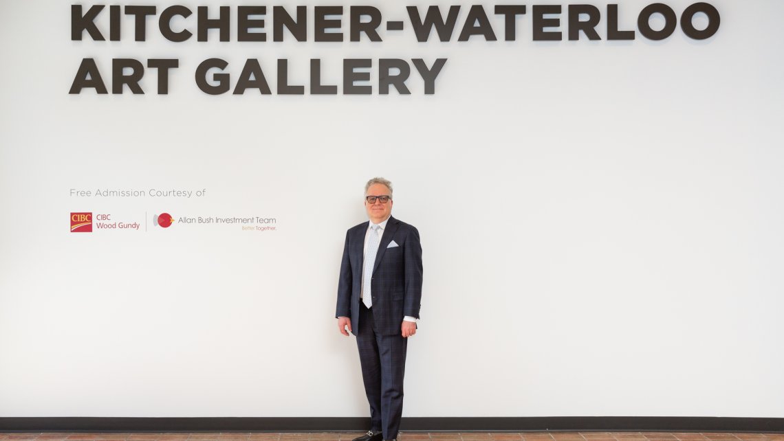 Photo of Allan Bush, an older man in a dark suit and glasses, standing alongside signage recognizing Free Admission Sponsor CIBC Wood Gundy - Allan Bush Investment Team
