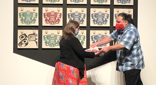 Luke Parnell hands a print from his installation to a woman in a black top and red skirt